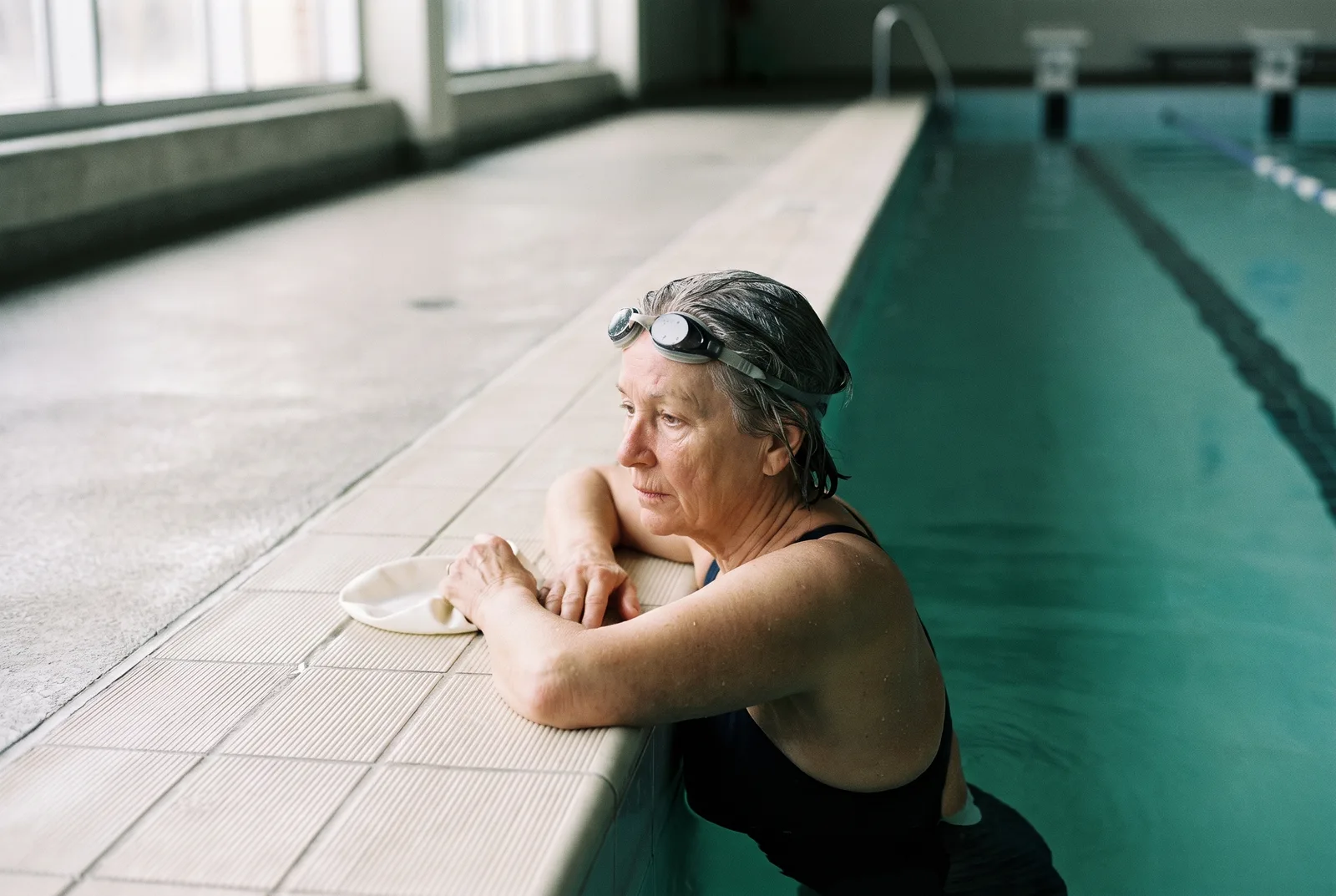 A woman at the edge of a pool after her swim, cap in hand, catching her breath.